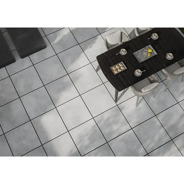 Terrassenfliese Dimension - 59,7 x 59,7 x 2 cm, Grau, Matt - Ein dunkler Gartentisch mit Stühlen auf einer Terrasse, perfekt für entspannte Stunden im Freien mit Getränken und Kuchen.