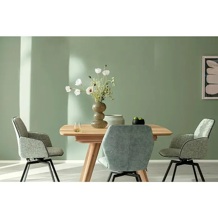 SCHÖNER WOHNEN-Farbe Wandfarbe Trendfarbe - Olive, Matt, 2,5 l, Konservierungsmittelfrei - Ein Esstisch aus Holz mit floralem Mittelstück und stilvollen Polsterstühlen vor einer grünen Wand.