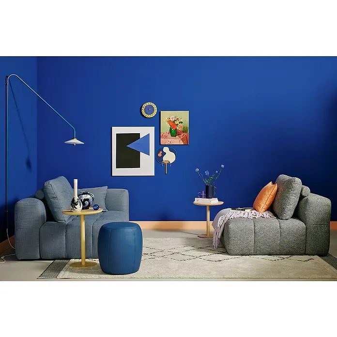SCHÖNER WOHNEN-Farbe Wandfarbe Trendfarbe Jubiläumsedition - Cornflower, Matt, 2,5 l, Konservierungsmittelfrei - Wohnzimmer mit blauem Farbschema, bestehend aus einem grauen Sessel, einem blauen Hocker und einem Couchtisch mit Dekorationsgegenständen.