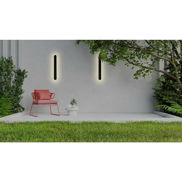 Searchlight LED-Außenwandleuchte Bordo - 12 W, 8 x 8 x 60 cm, IP65 - Eine moderne Außenwandleuchte in Schwarz erhellt eine Terrasse mit einem Sessel, einem Tisch und üppigem Grün.
