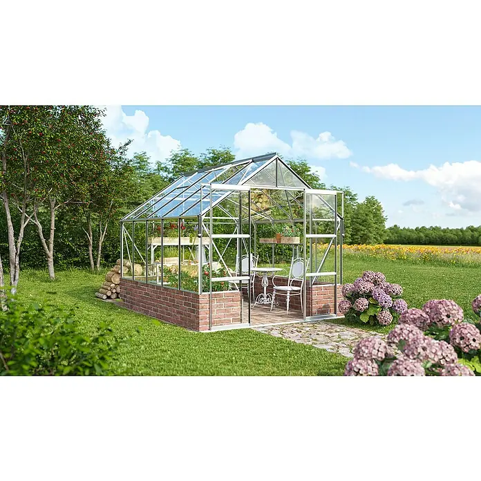 Vitavia Gewächshaus Cassandra 8300 - Außenmaß inkl. Dachüberstand (B x T): 257 x 323 cm, 3 mm, Aluminium - Ein schönes Gewächshaus mit Glaswänden und einem Backsteinsockel steht in einem grünen Garten mit Blumen und Bäumen.