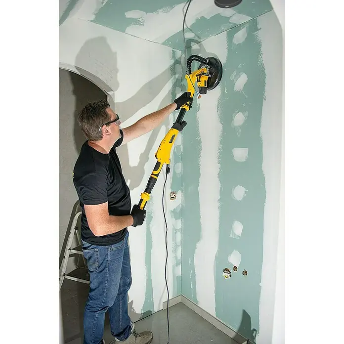 PowerPlus Lijadora de pared y techo POWX04761 - 710 W, Diámetro disco de lija: 225 mm - Un hombre utiliza una lijadora de paneles de yeso Menzer para preparar una pared. La herramienta tiene un mango largo y un cabezal de lijado.