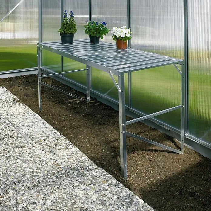 Vitavia Gewächshaus Cassandra 11500 Plus - Außenmaß inkl. Dachüberstand (B x T): 257 x 448 cm, 3 mm, Aluminium - Silberner Pflanztisch im Gewächshaus mit drei Blumentöpfen darauf. Perfekt für die Aufzucht von Pflanzen und Gemüse im eigenen Garten.