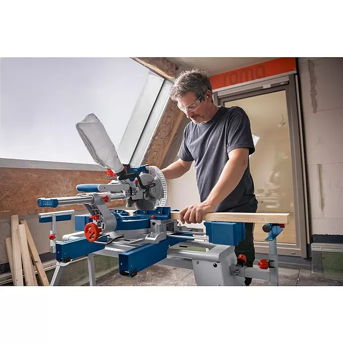 Bosch Professional AMPShare 18V Akku-Kapp- & Gehrungssäge GCM 18V-216 D - 18 V, Ohne Akku, 5.000 U/min - Mann schneidet ein Holzbrett mit einer blau-grauen Bosch Kappsäge, trägt Schutzbrille und Gehörschutz.