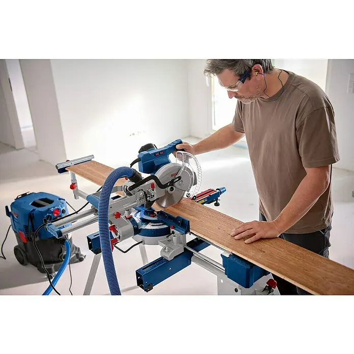 Bosch Professional Kapp- & Gehrungssäge GCM 305-216 D - 1.200 W, Durchmesser Sägeblatt: 216 mm, Leerlaufdrehzahl: 5.200 U/min - Ein Mann bedient eine Bosch Kapp- und Gehrungssäge mit Staubabsaugung, um ein Holzbrett präzise zu schneiden, während er Schutzkleidung trägt.