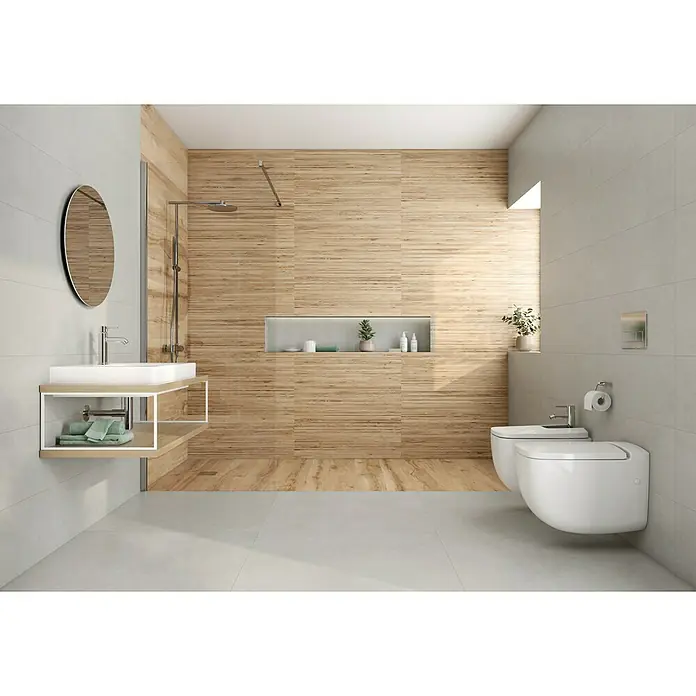 Revestimiento de pared Logan - 30 x 90,2 cm, Gris, Mate, Rectificado - Un baño moderno con azulejos imitación madera, espejo redondo sobre el lavabo y un inodoro suspendido.