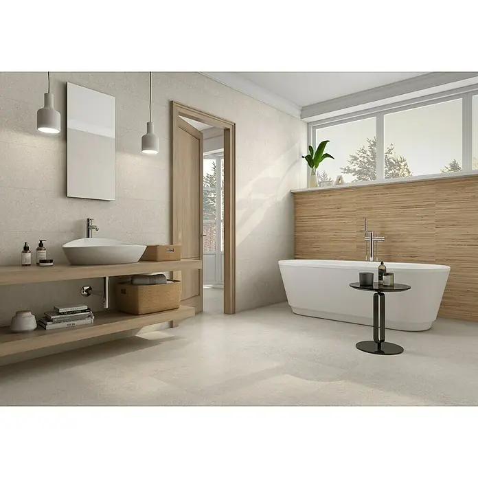 Revestimiento de pared Yafra - 30 x 90,2 cm, Arena, Mate, Rectificado - Luminoso baño con bañera, tocador con lavabo sobre encimera, espejo y detalles de madera, creando un ambiente elegante y relajante.