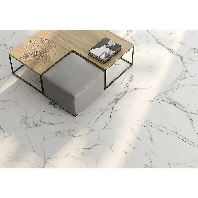 BHS Showroom Pavimento porcelánico Carrara - 90 x 90 cm, Blanco, Mate, Rectificado - Vista de una mesa de centro cuadrada con acabado de madera y un cubo de asiento gris, sobre elegantes baldosas de mármol.