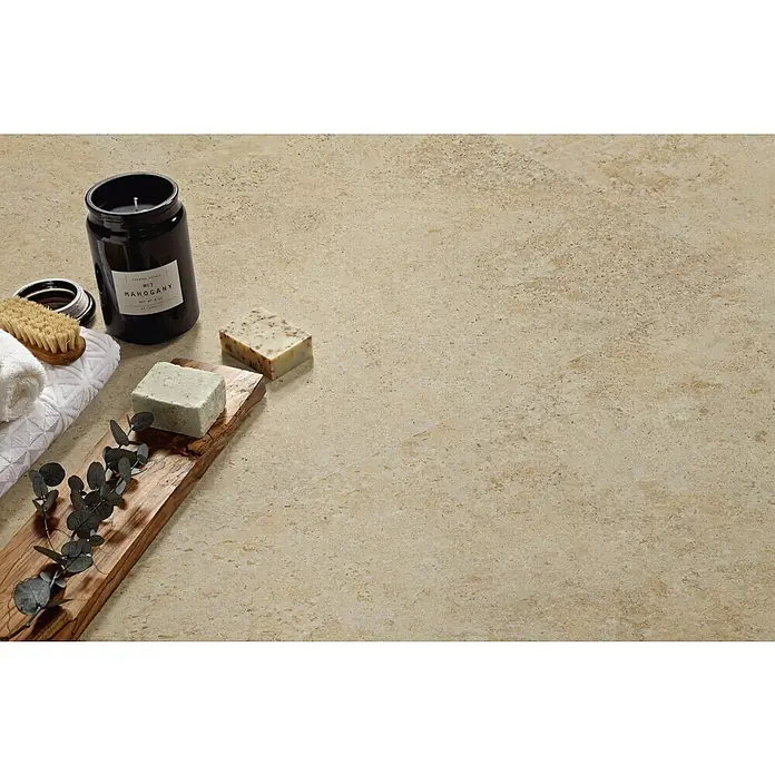 Pavimento porcelánico Ostuni - 60 x 60 cm, Beige, Mate, Rectificado - Primer plano de un lujoso juego de baño con vela, jabón, toalla y cepillo sobre una encimera beige.
