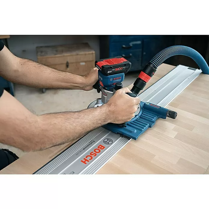 Bosch Professional AMPShare 18V Akku-Kantenfräser GKF 18V-8 - 18 V, Anzahl Akkus: Ohne Akku, Leerlaufdrehzahl: 10.000 U/min - 30.000 U/min - Eine Person bedient einen blauen und roten Bosch Akku-Fräser auf einer Holzoberfläche, geführt von einer silbernen Schiene mit blauem Absaugschlauch.