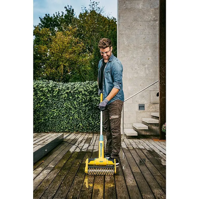 Gloria Bodenreinigungsbürste Multibrush XL - 500 W, Arbeitsbreite: 32 cm, Höhenverstellung: 115 cm - 135 cm - Ein Mann reinigt eine Holzterrasse mit der Gloria MultiBrush XL, einer gelben Bürste mit Teleskopstiel für die Außenreinigung.