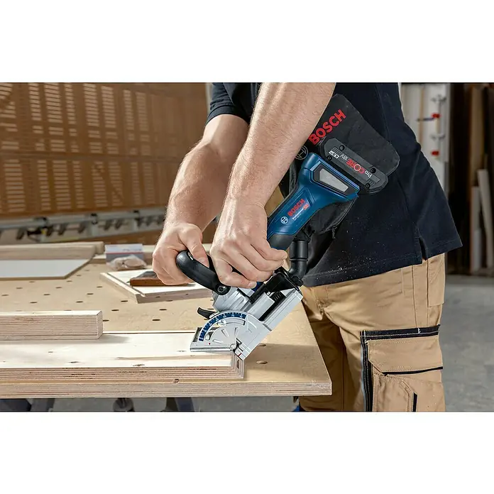 Bosch Professional AMPShare 18V Akku-Flachdübelfräse GFF 18V-22 - 18 V, Ohne Akku, Leerlaufdrehzahl: 11.000 U/min - Eine Bosch Akku-Nutfräse wird zum Bearbeiten eines Holzstücks verwendet. Der Arbeiter trägt Arbeitskleidung.