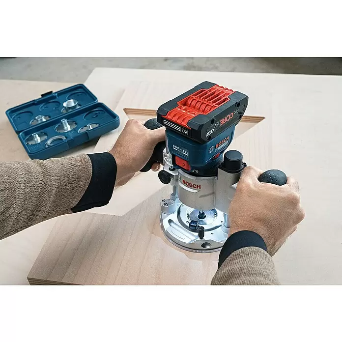 Bosch Professional AMPShare 18V Akku-Kantenfräser GKF 18V-8 - 18 V, Anzahl Akkus: Ohne Akku, Leerlaufdrehzahl: 10.000 U/min - 30.000 U/min - Hände führen eine blaue und schwarze Bosch Akku-Oberfräse mit rotem Akku, die helles Holz bearbeitet. Eine blaue Zubehörbox liegt im Hintergrund.