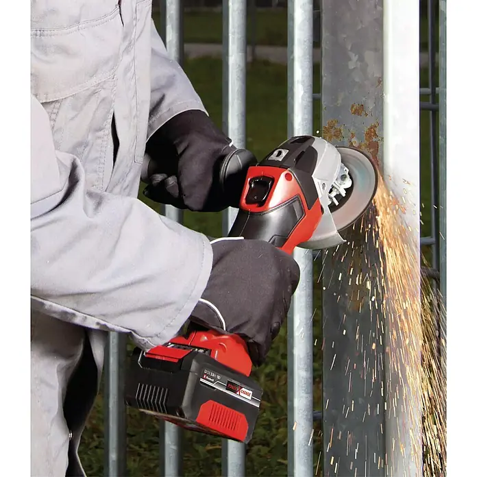 Einhell PXC 18V Amoladora angular de batería TC-AG 18/115 Li - 18 V, 1 batería, 4 Ah, Diámetro disco: 115 mm - Un trabajador está usando una amoladora angular inalámbrica Einhell para quitar el óxido de una valla metálica. Las chispas vuelan durante el rectificado.