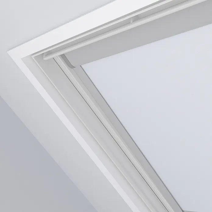 Dachfensterrollo Sky UK08 - Weiß, Manuell - Nahaufnahme eines Dachfensters mit Rollo, das sanftes Licht in den Raum lässt. Das Rollo ist in einem schlichten Weiß gehalten, passend zum Rahmen.