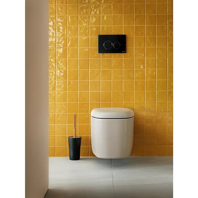 VitrA Plural Wand-WC - Spülrandlos, Mit schmutzabweisender Glasur, Spülform: Tief, WC Abgang: Waagerecht, Taupe - Wandmontiertes WC mit Spülkasten und Toilettenbürste vor gelben Fliesen.