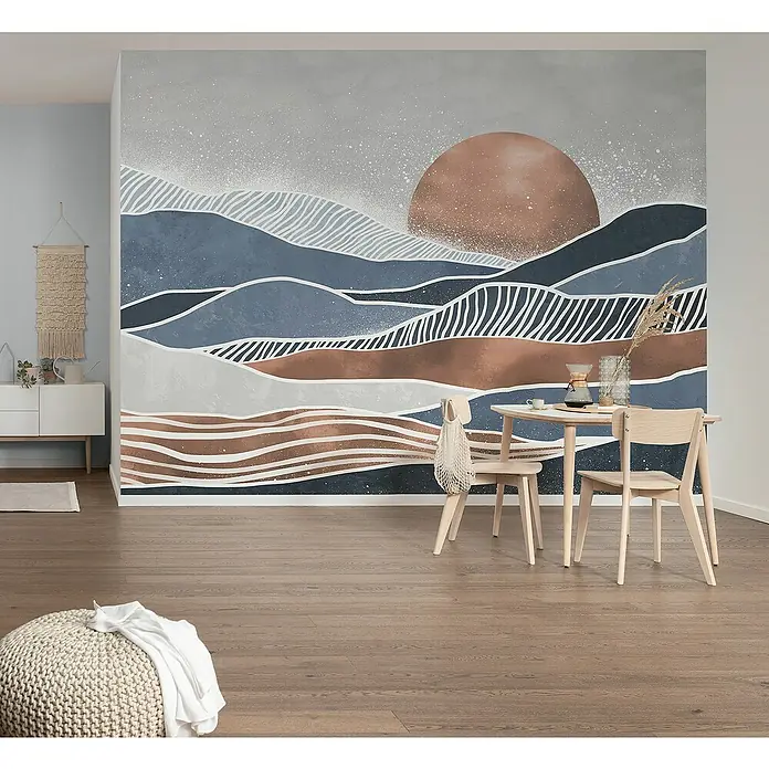 Komar Flair Fototapete Shades of Greece - B x H: 350 x 250 cm, Vlies - Ein stilvolles Interieur mit einem Wandbild, das eine abstrakte Berglandschaft bei Sonnenaufgang zeigt, und hellen Holzmöbeln.