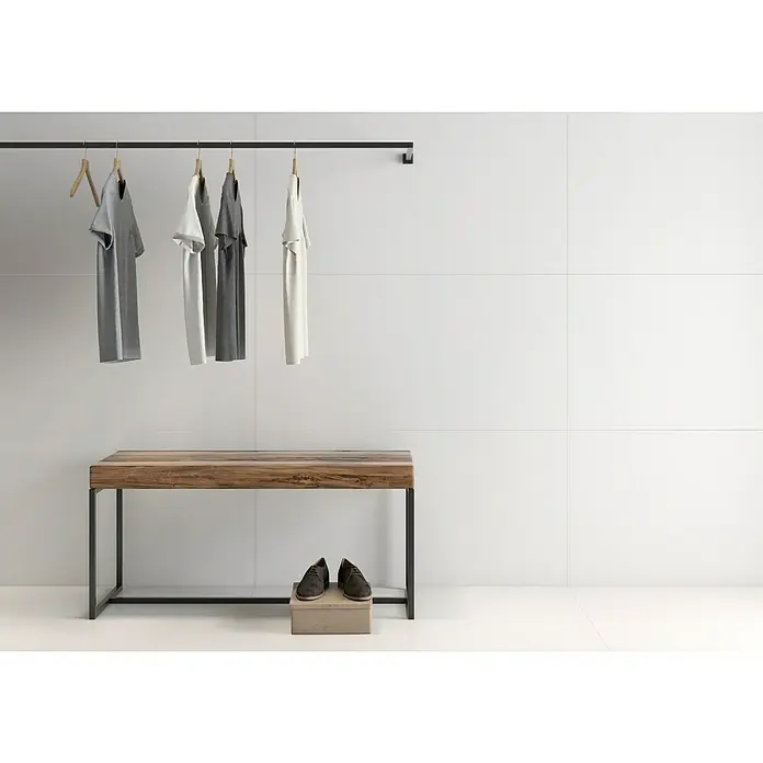 Pavimento porcelánico Fresh - 60 x 120 cm, Blanco, Mate, Rectificado - Armario minimalista con ropa en una barra, un banco de madera y zapatos en una caja, sobre una pared blanca.