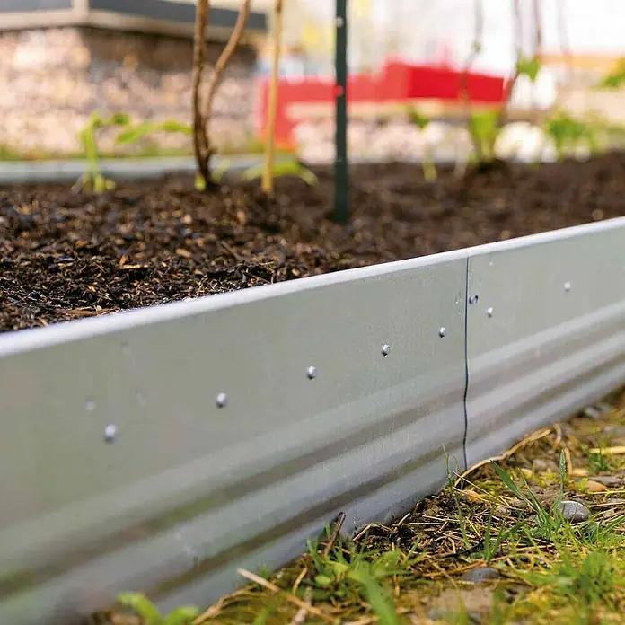Bellissa Beeteinfassung Pro - 103 x 13 cm, Stahl - Nahaufnahme eines erhöhten Metallgartenbeets mit dunkler Erde und grüner Vegetation im Hintergrund.