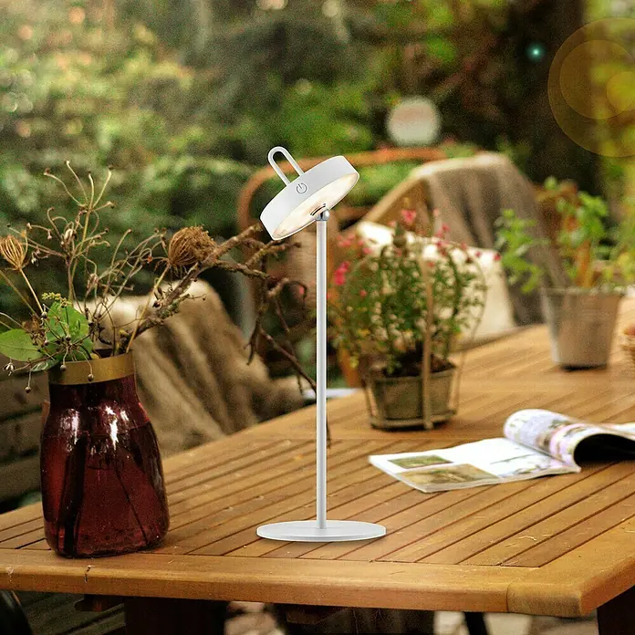 Paul Neuhaus Lámpara de sobremesa LED Amag - 1,5 W, L x An x Al: 15 x 15 x 47,2 cm, Blanco, Blanco cálido - Una lámpara de mesa LED inalámbrica con una pantalla redonda y un elegante soporte plateado, exhibida sobre una mesa de madera al aire libre.