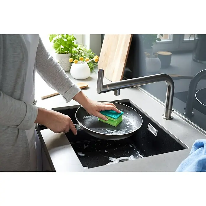 Vileda Glitzi Topfreiniger Sauber & Hygienisch Ultra Fresh 3+1 - 4 Stk. - Eine Person spült eine Bratpfanne mit einem grünen Schwamm in einem modernen Spülbecken, während Pflanzen im Hintergrund stehen.