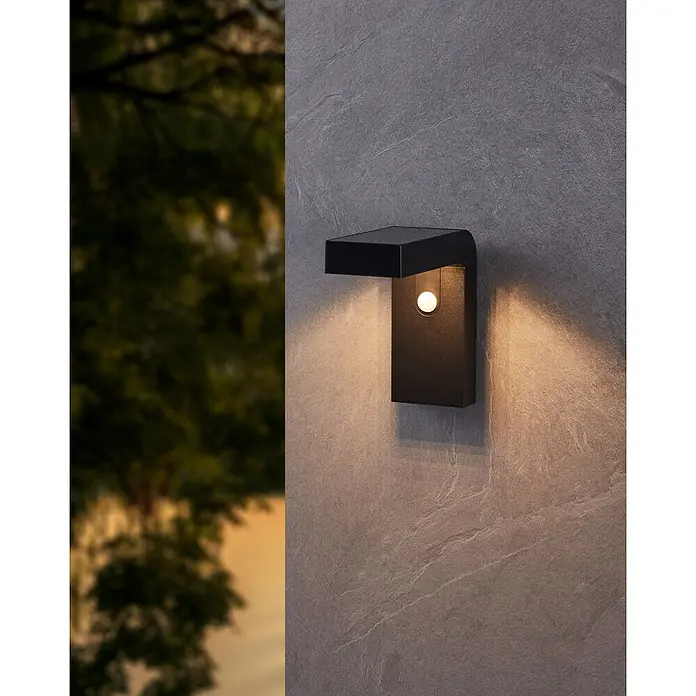 Eglo Aplique solar para exterior Baracconi - 18 W, Negro, IP44, 300 lm - Primer plano de una lámpara de pared negra con un brillo cálido, montada en una pared exterior texturizada.