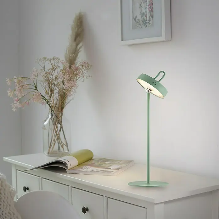 Paul Neuhaus Lámpara de sobremesa LED Amag - 1,5 W, L x An x Al: 15 x 15 x 47,2 cm, Verde, Blanco cálido - Una lámpara de mesa verde con un diseño moderno está sobre una cómoda, junto a un jarrón con flores. La lámpara proporciona una luz agradable.