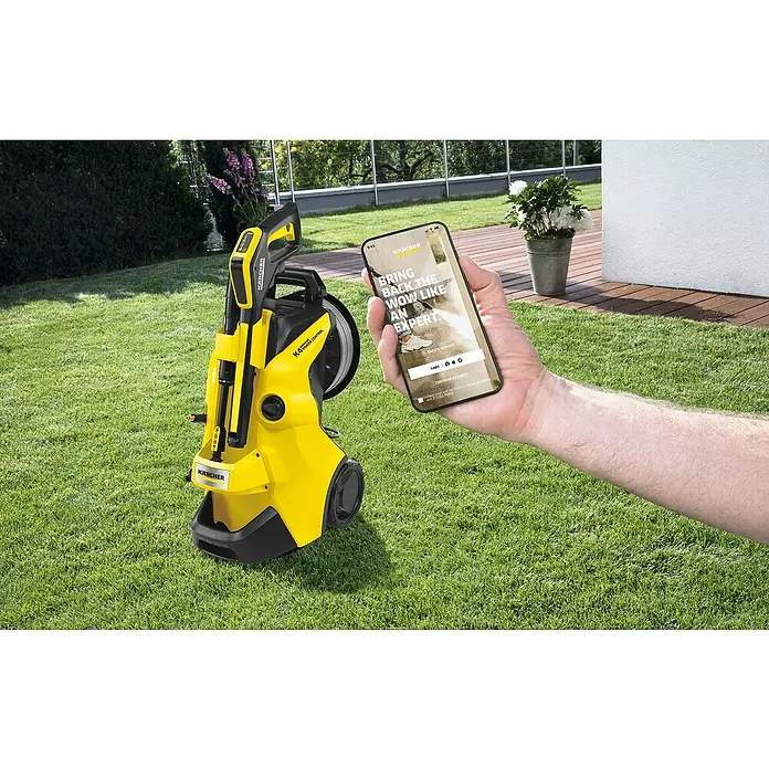 Kärcher Hidrolimpiadora de alta presión K 4 Premium Power Control Flex - 130 bar, 1.800 W, Capacidad de bombeo: 420 l/h - Hidrolimpiadora amarilla Kärcher K4 Power Control sobre césped con un teléfono móvil en la mano que muestra la app Kärcher.