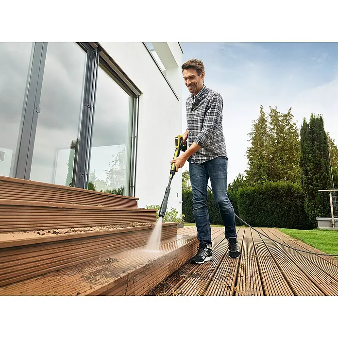Kärcher Hochdruckreiniger K 5 Power Control Flex - 145 bar, 2.100 W, Fördermenge: 500 l/h, Ohne Home Kit - Ein Mann benutzt einen Kärcher Hochdruckreiniger, um eine Holzterrasse zu säubern, wobei der Fokus auf dem Kärcher Gerät liegt.