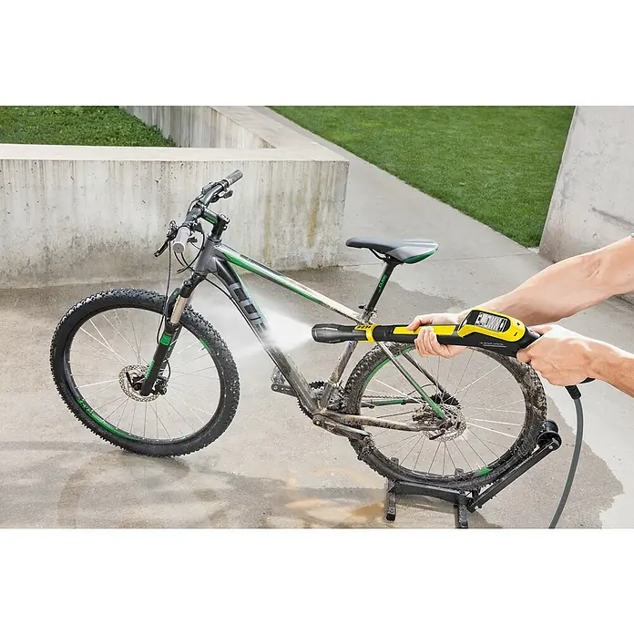 Kärcher Hidrolimpiadora de alta presión K 7 Smart Control Flex - 180 bar, 3.000 W, Capacidad de bombeo: 600 l/h, Sin Home Kit - Se está limpiando una bicicleta con una limpiadora de alta presión Kärcher. El Kärcher es amarillo y negro y está operado por una persona.