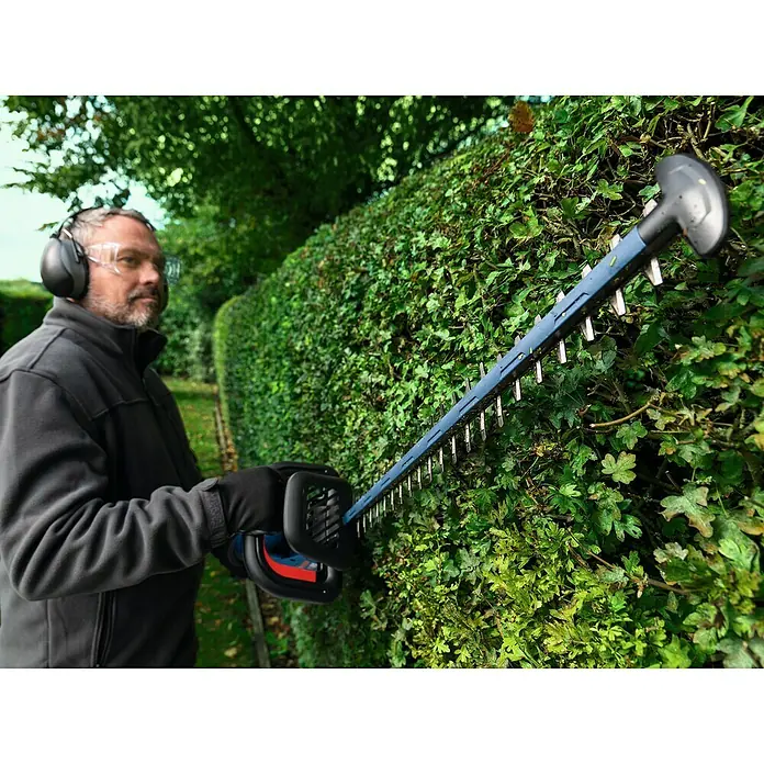Bosch Professional AMPShare 18V Akku-Heckenschere GHE 18V-60 II - 18 V, Ohne Akku, Schwertlänge: 60 cm - Ein Gärtner schneidet eine Hecke mit einer Bosch Heckenschere, umgeben von viel Grün und natürlichem Licht.