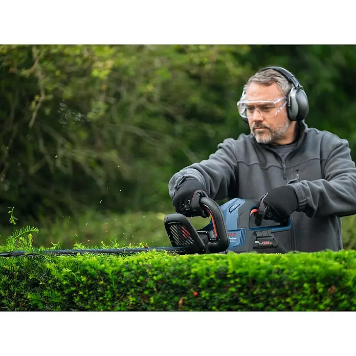 Bosch Professional AMPShare 18V Akku-Heckenschere GHE 18V-60 II - 18 V, Ohne Akku, Schwertlänge: 60 cm - Ein Mann trimmt eine Hecke mit einer Bosch Akku-Heckenschere und trägt dabei Sicherheitsausrüstung.