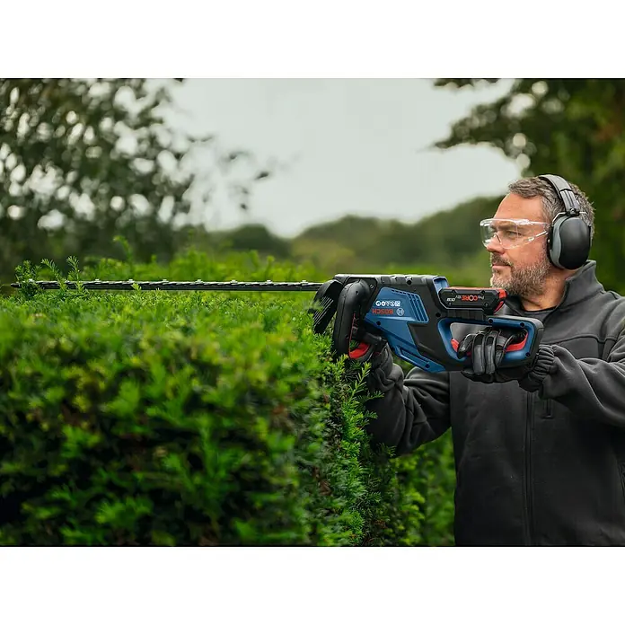 Bosch Professional AMPShare 18V Akku-Heckenschere GHE 18V-60 II - 18 V, Ohne Akku, Schwertlänge: 60 cm - Ein Mann schneidet eine Hecke mit einer Bosch Akku-Heckenschere. Die Heckenschere ist blau und hat einen schwarzen Schneidkopf.