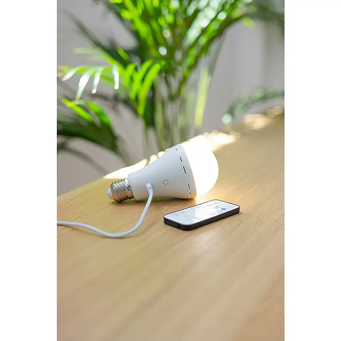 New Garden Bombilla LED recargable Lapera - E27, Intensidad regulable, Blanco cálido, 350 lm, 3,5 W - Una bombilla LED E27 recargable con control remoto sobre la mesa, ideal para emergencias y uso diario.