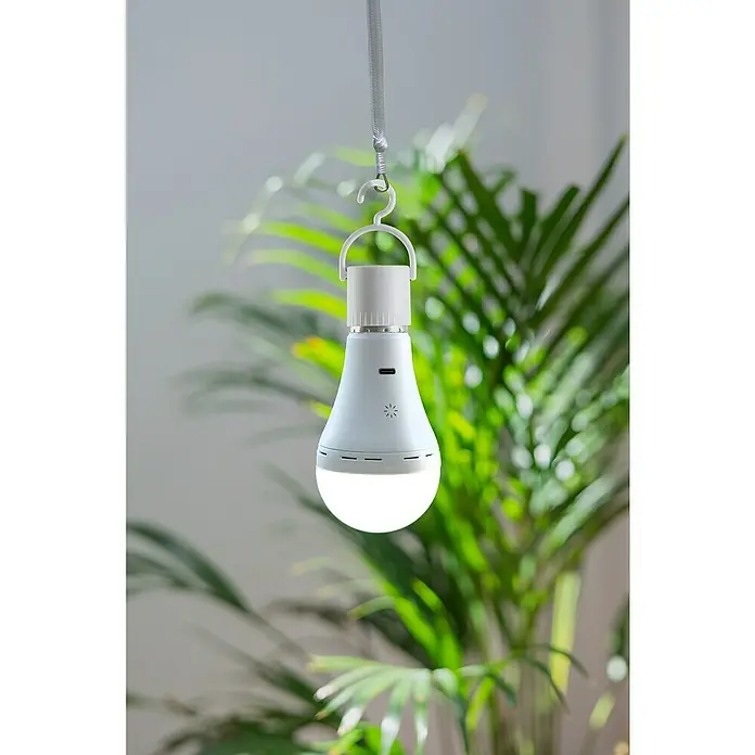 New Garden Bombilla LED recargable Lapera - E27, Intensidad regulable, Blanco cálido, 350 lm, 3,5 W - Primer plano de una bombilla LED colgante que emite una luz cálida, con un fondo de vegetación exuberante.