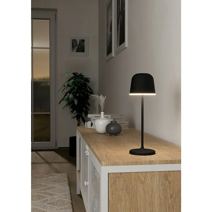 Eglo Lámpara de sobremesa a batería Mannera - Ø x Al: 11 x 34 cm, Negro, 2,2 W, IP54 - Elegante lámpara de mesa inalámbrica negra que emite un brillo cálido, mostrada sobre un gabinete de madera. Ideal como luz de acento.