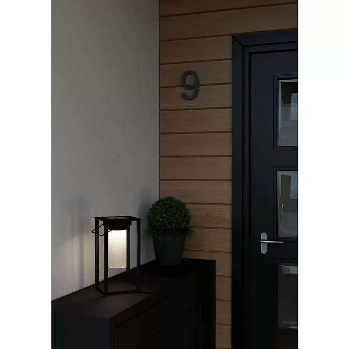 Eglo Lámpara de sobremesa solar Usigni - 2,5 W, L x An x Al: 15 x 15 x 28 cm, Negro, IP44 - Moderna linterna de metal negro con luz blanca brillante sobre un mueble oscuro, junto a una planta, en la entrada de una casa.