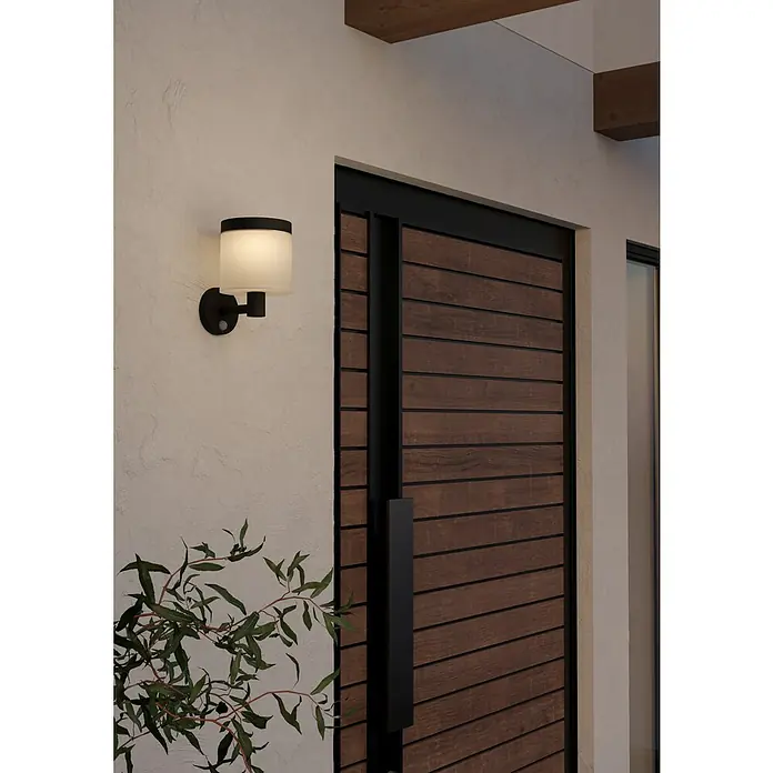 Eglo Aplique solar LED para exterior Pantete - 8 W, Plástico, Blanco cálido, Negro - Una moderna lámpara de pared exterior negra con pantalla cilíndrica junto a una puerta de madera. Diseño simple para la entrada.