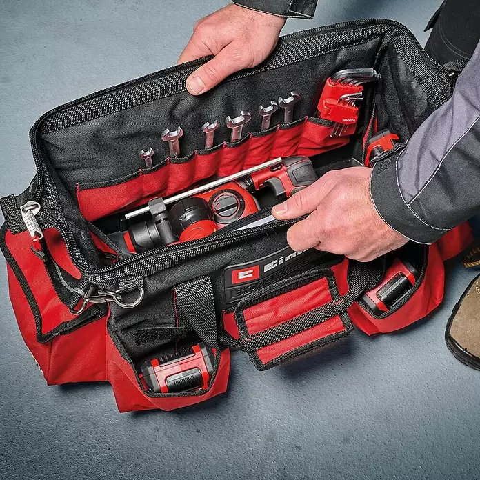 Einhell Werkzeugtasche E-Case - L x B x H: 26,4 x 13,5 x 49 cm, Traglast: 30 kg - Hände öffnen eine rot-schwarze Werkzeugtasche, die geordnete Schraubenschlüssel und Elektrowerkzeuge zeigt.