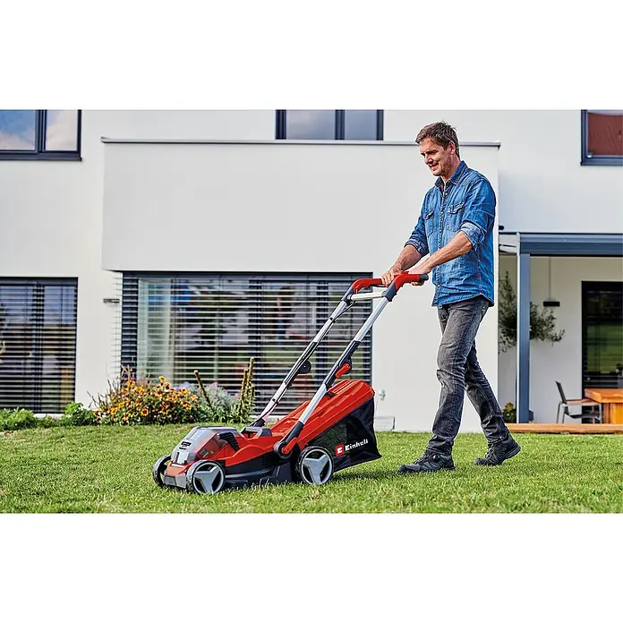 Einhell Power X-Change 18V Akku-Rasenmäher Rasarro 36/34 - 36 V, 2 Akkus, 3 Ah, Schnittbreite: 34 cm - Mann mäht Rasen mit einem roten Einhell Rasenmäher im Garten eines modernen Hauses.