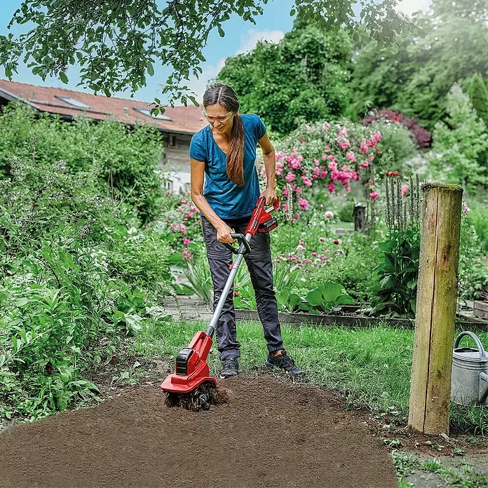 Einhell Power X-Change 18V Akku-Bodenhacke GE-CR 18/20LI E - Anzahl Akkus: Ohne Akku, Li-Ionen - Frau lockert Erde mit roter und grauer Motorhacke in einem grünen Garten.