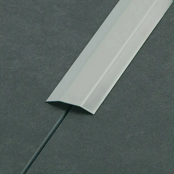 Perfil de transición - Acero, Plateado - Primer plano de una tira de umbral plateada sobre una superficie oscura, que proporciona una transición limpia entre dos materiales de piso.