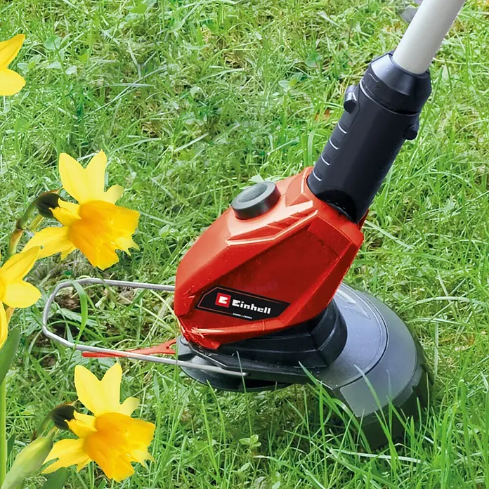 Einhell Power X-Change 18V Akku-Rasentrimmer GE-CT 18 Li - 18 V, 2,5 Ah, Li-Ionen, 1 Akku, Schnittbreite Messer: 24 cm - Ein roter Einhell Rasentrimmer steht im Gras, neben gelben Narzissen. Das Gerät ist bereit zum Trimmen und zur Rasenpflege im Garten.