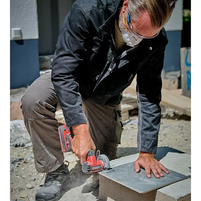 Einhell Professional Power X-Change 18V Akku-Trennschleifer TP-CO 18/76-C Li BL - Solo - Ohne Akku - Rote Akku-Handkreissäge schneidet eine graue Fliese.