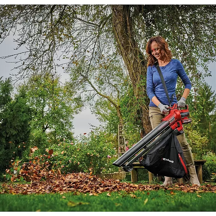 Einhell Power X-Change 18V Akku-Laubsauger & -Laubbläser Venturro 18/210 - 18 V, Ohne Akku, Blasgeschwindigkeit: 210 km/h - Frau nutzt roten und schwarzen Einhell Akku-Laubbläser/Sauger, um Blätter im Garten zu entfernen.