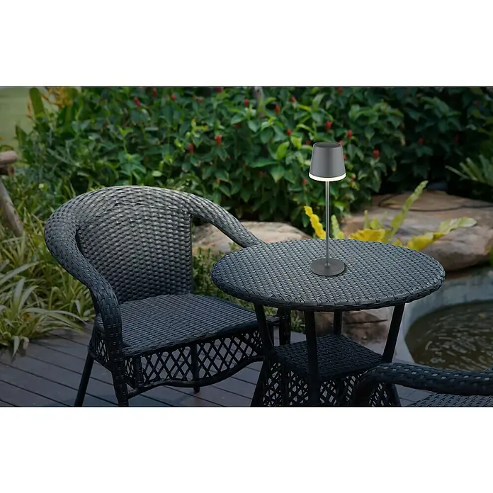 Globo Solar-Tischleuchte - Schwarz, Warmweiß, IP44, Ø x H: 11 x 41 cm - Eine stilvolle Szene mit einem modernen Outdoor-Tischlampe auf einem Tisch, umgeben von geflochtenen Gartenmöbeln und üppigem Grün.