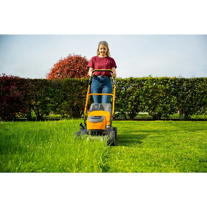 Stiga Akku-Rasenmäher Collector 48 AE Kit - 48 V, 1 Akku, 4 Ah, Schnittbreite: 46 cm - Eine Frau mäht den Rasen mit einem gelben Rasenmäher vor einer grünen Hecke und einem roten Busch im Hintergrund.
