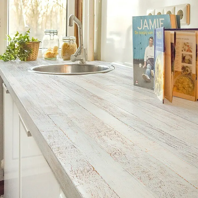 Lámina decorativa autoadhesiva vinílico para encimera - 65 x 200 cm, Saloon - Primer plano de una encimera de cocina con fregadero, grifo, libros de cocina y planta en maceta, mostrando una configuración de cocina acogedora y funcional.