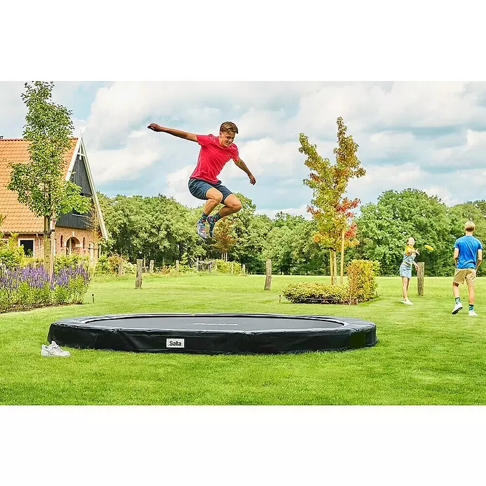 Salta Trampolin Premium Ground - Durchmesser: 396 cm, Schwarz - Schwarzes Bodentrampolin, eine Person springt hoch darauf.