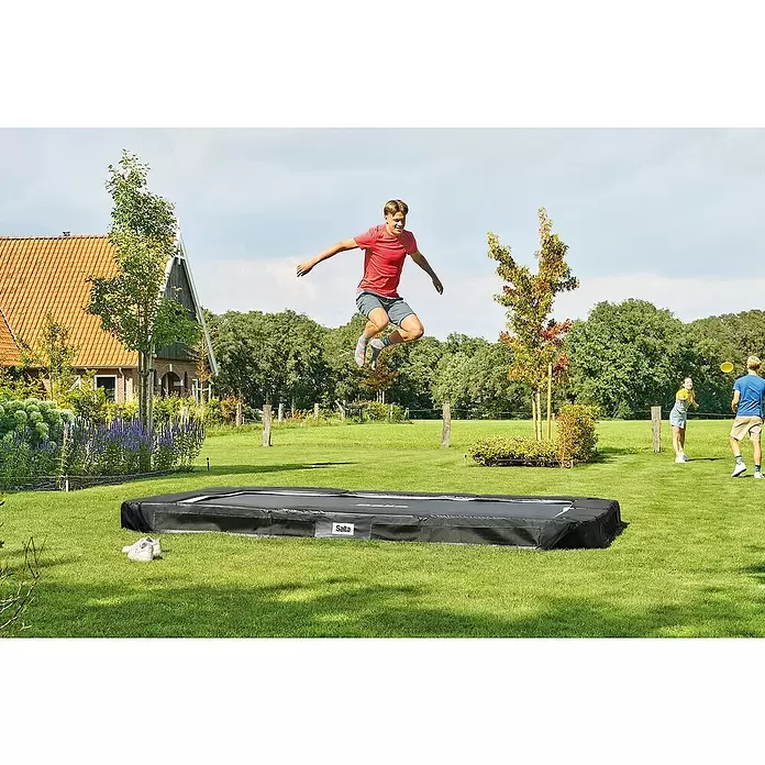 Salta Trampolin Premium Ground - B x L: 214 x 305 cm, Schwarz - Schwarzes rechteckiges Salta Trampolin ebenerdig im grünen Rasen, eine Person springt darauf.